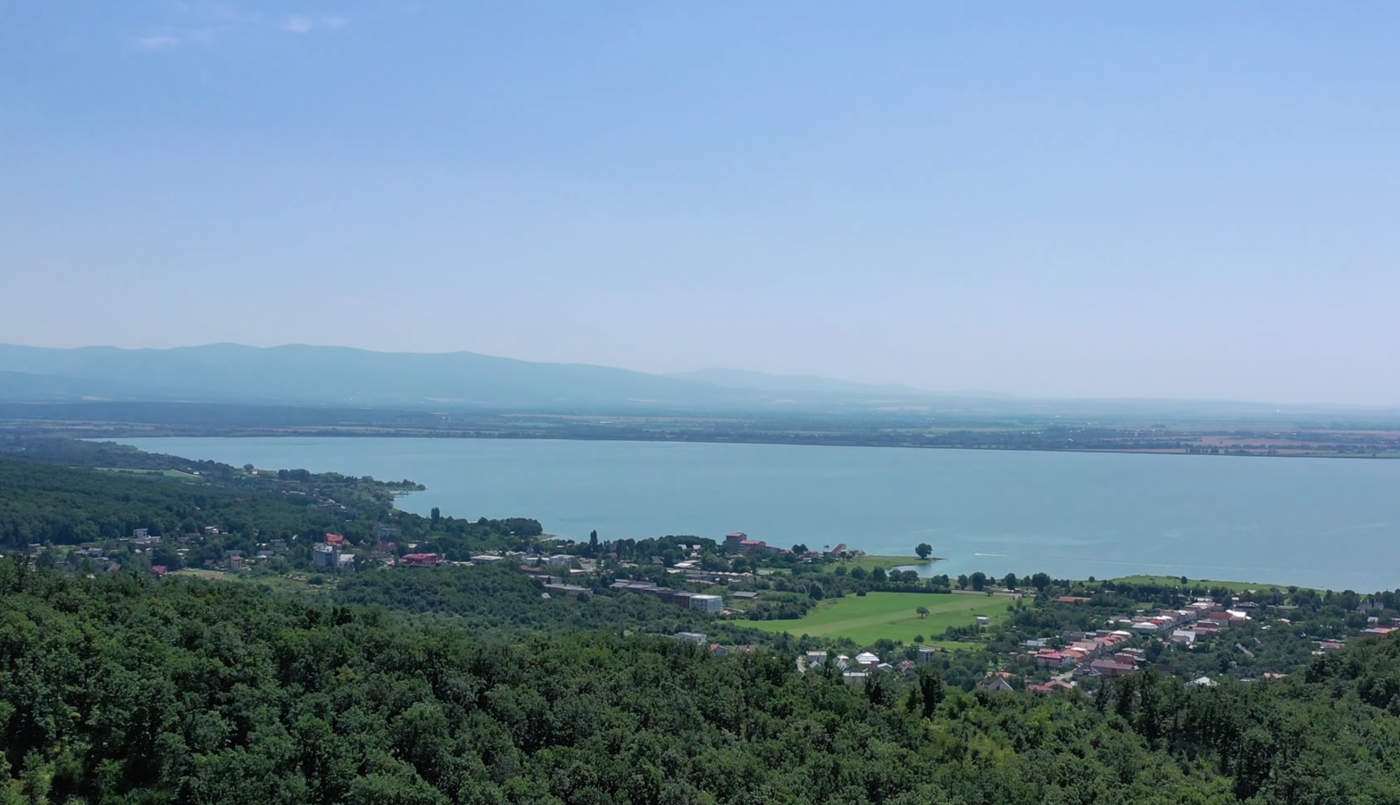 Panoramatický pohľad na Zemplínsku šíravu z Vihorlatu s obcami na brehu a horami v pozadí