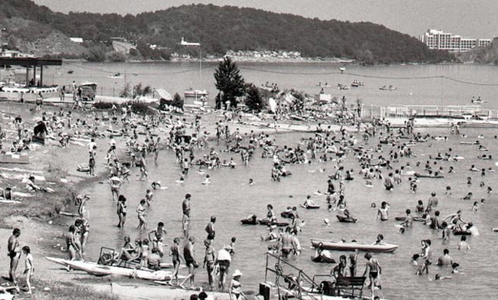 Preplnená pláž na Zemplínskej šírave v 70. alebo 80. rokoch – stovky rekreantov pri vode s hotelmi na kopci v pozadí